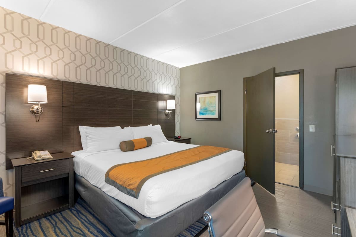 A hotel room with a large bed, a nightstand with a lamp, a painting on the wall, and a door leading to a bathroom.
