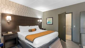 Une chambre d’hôtel avec un grand lit, une table de chevet avec une lampe, un tableau au mur et une porte donnant sur une salle de bain.