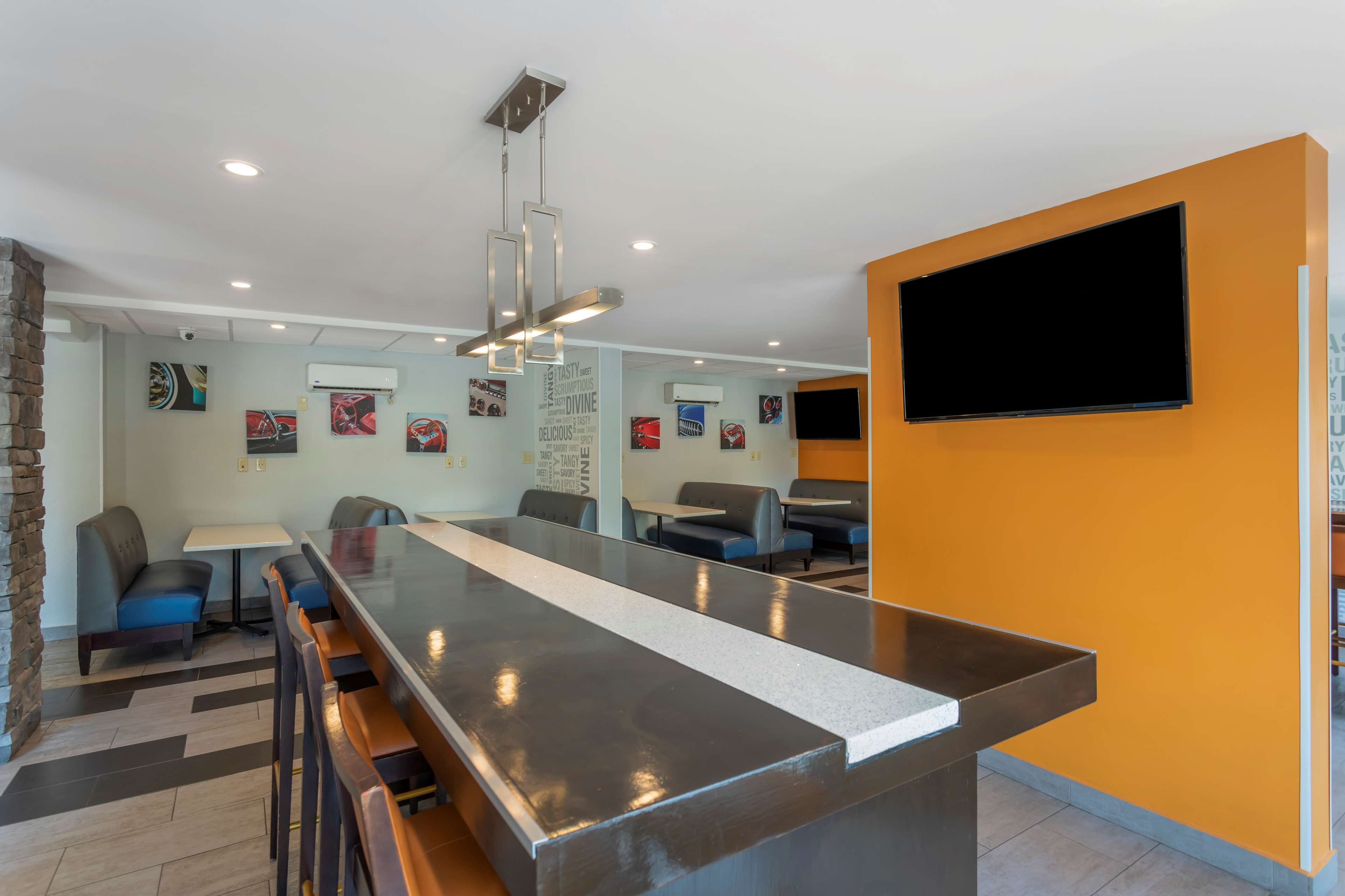 A modern restaurant with a long counter, bar stools, and a TV mounted on the wall.