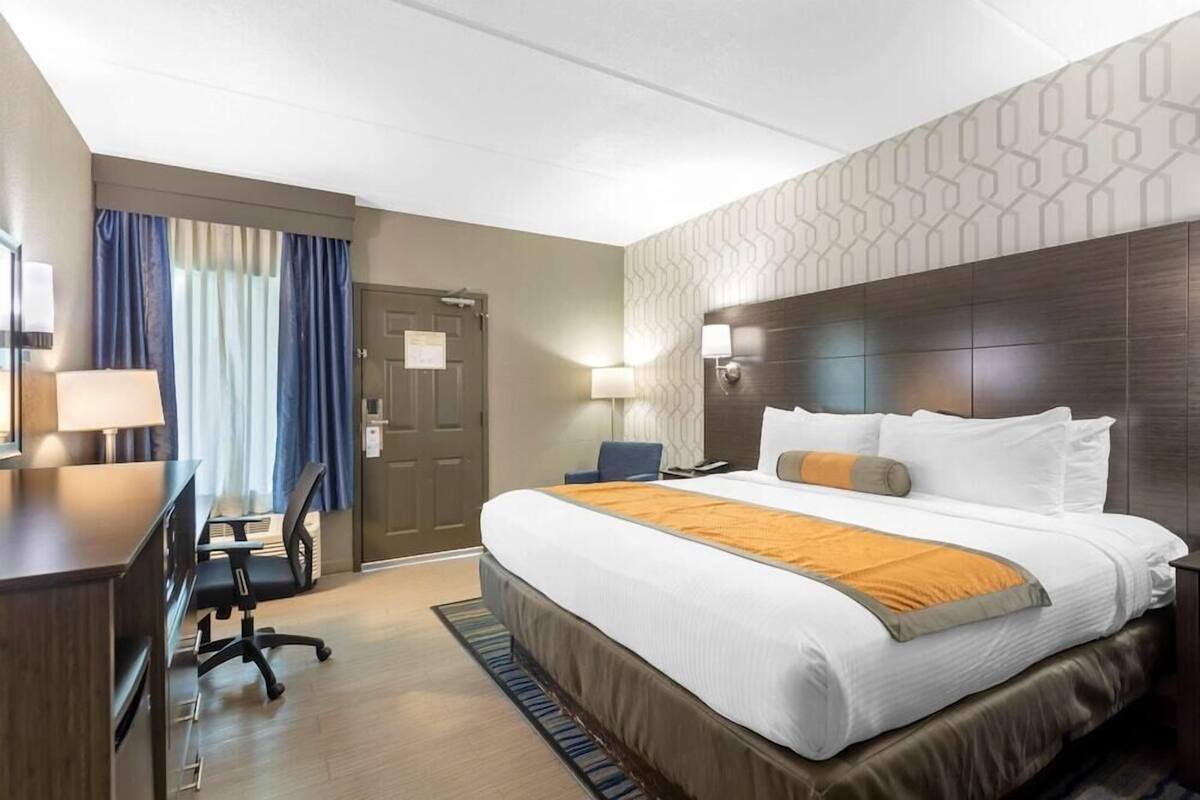 A hotel room with a bed, desk, chair, and lamps.