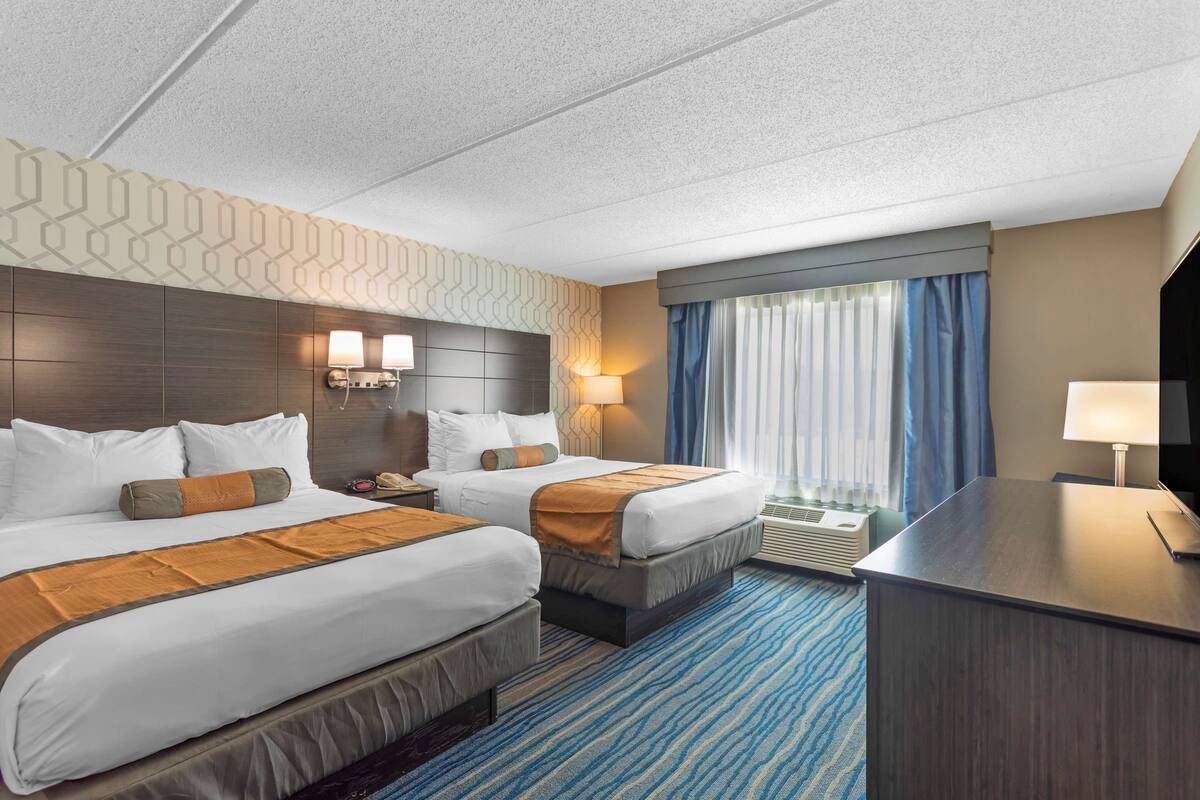A hotel room with two beds, a desk, a nightstand, and a large window with curtains.