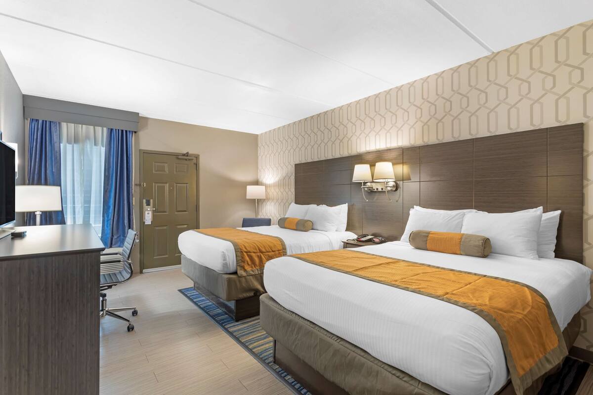 A hotel room with two beds, a desk, a chair, a TV, and a door.