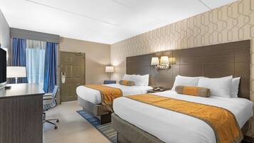 Ein Hotelzimmer mit zwei Betten, einem Schreibtisch, einem Stuhl, einem Fernseher und einer Tür.