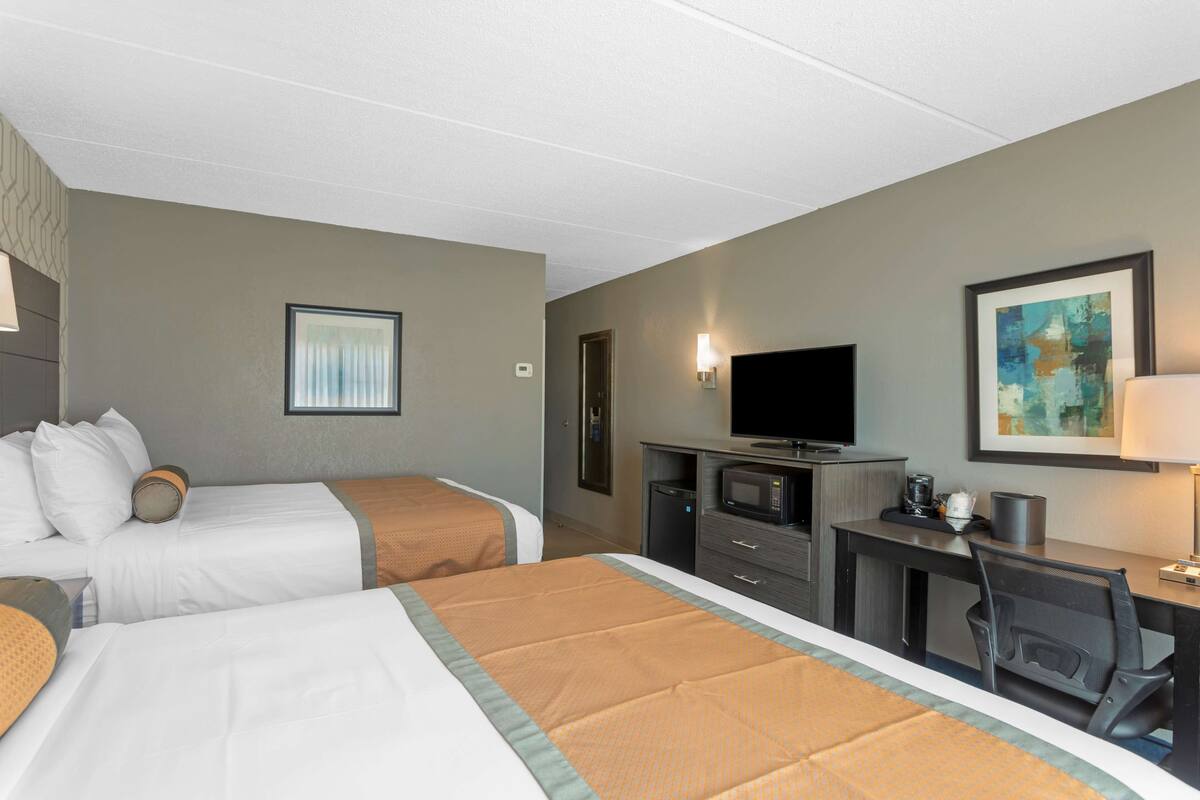 A hotel room with two beds, a desk with a chair, a television, and a painting on the wall.