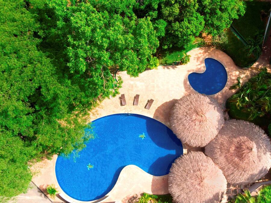 A circular pool with three lounge chairs and a thatched umbrella.