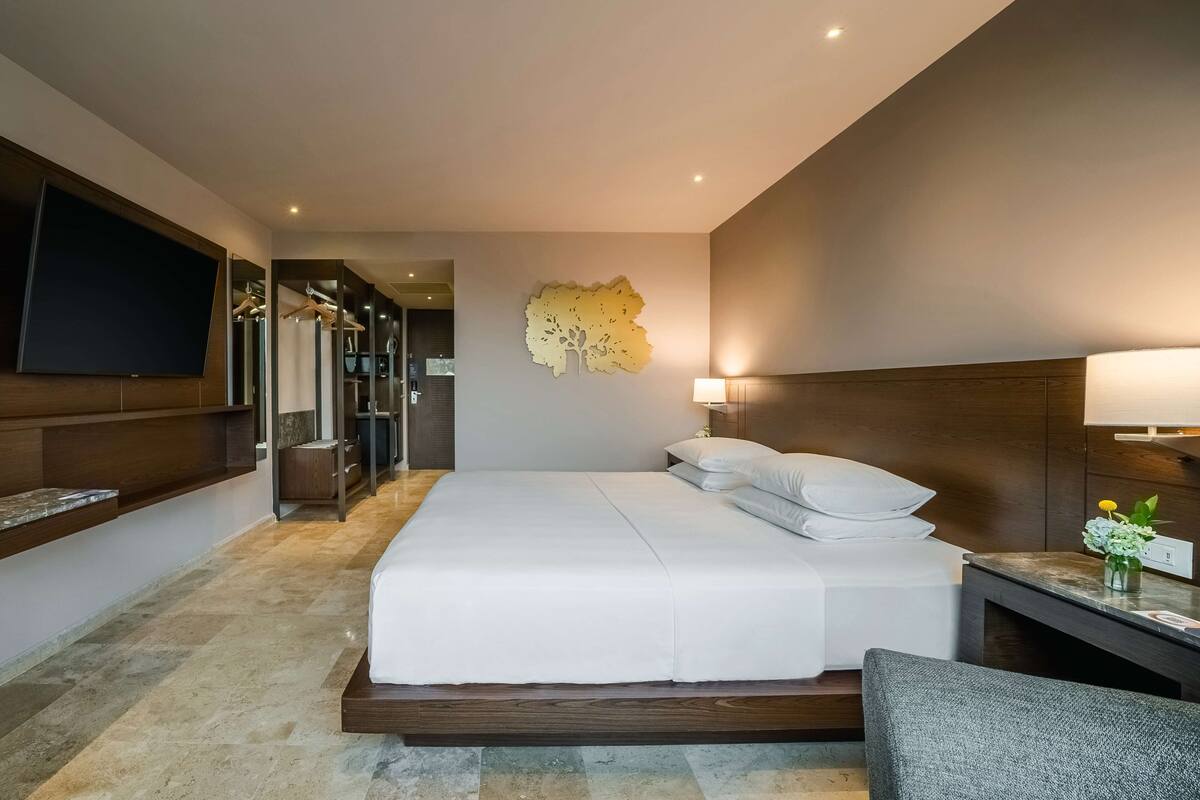 A modern hotel room with a large bed, a flat-screen TV mounted on the wall, and a wooden headboard.