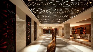 Un hall d’entrée moderne avec une sculpture centrale en bois, des murs aux motifs décoratifs et un plafond orné de découpes géométriques.