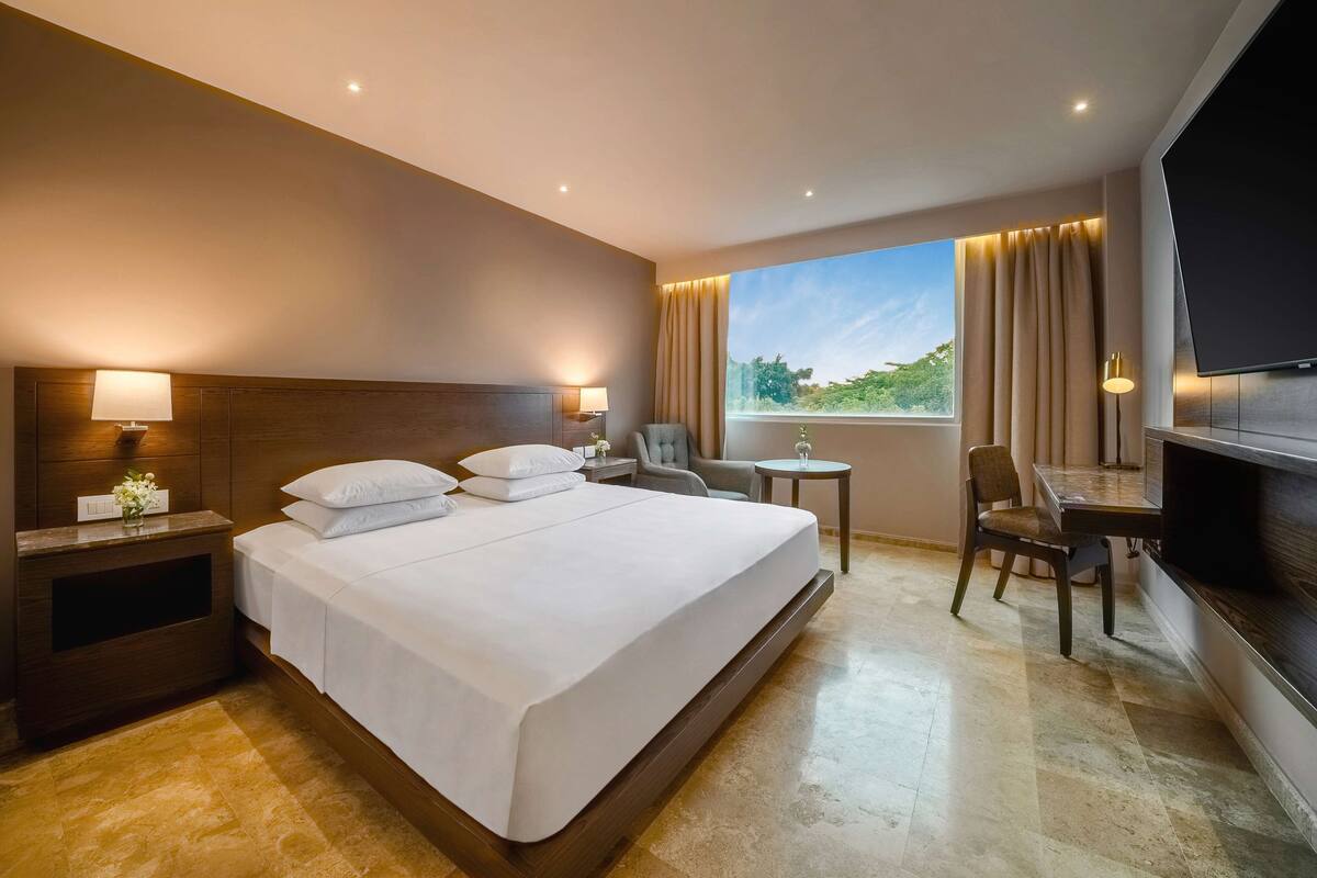 A hotel room with a large bed, bedside tables, a TV, a small table, and a chair.