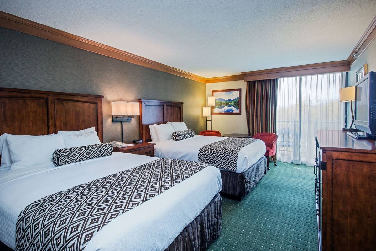 Une chambre d’hôtel avec deux lits, un bureau, une chaise, une télévision et une fenêtre avec des rideaux.