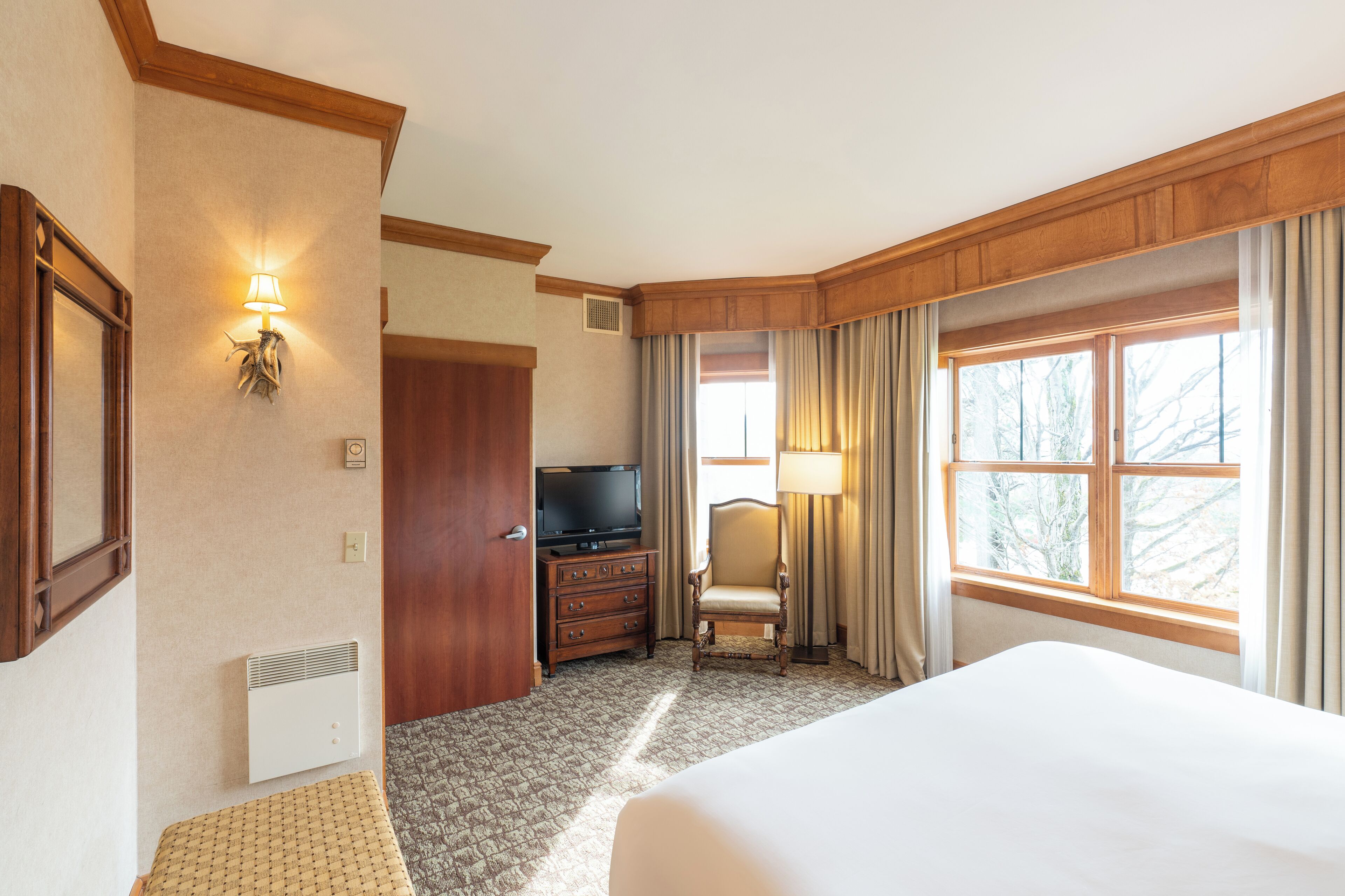 Une chambre d’hôtel avec un grand lit, une télévision, une commode, une chaise et une fenêtre avec des rideaux.
