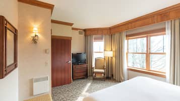 Een hotelkamer met een groot bed, een televisie, een dressoir, een stoel en een raam met gordijnen.