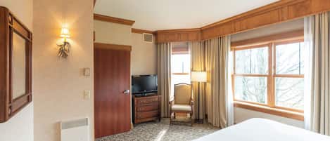 A hotel room with a large bed, a television, a dresser, a chair, and a window with curtains.