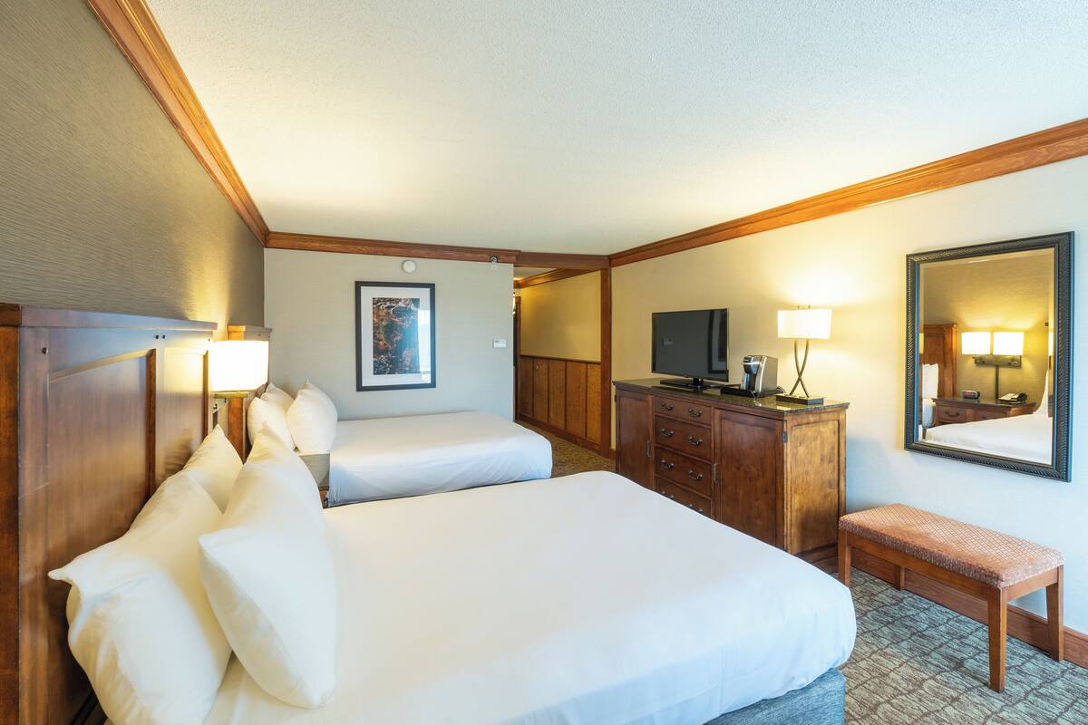 Une chambre d’hôtel avec deux lits, une commode en bois, un téléviseur et un banc.
