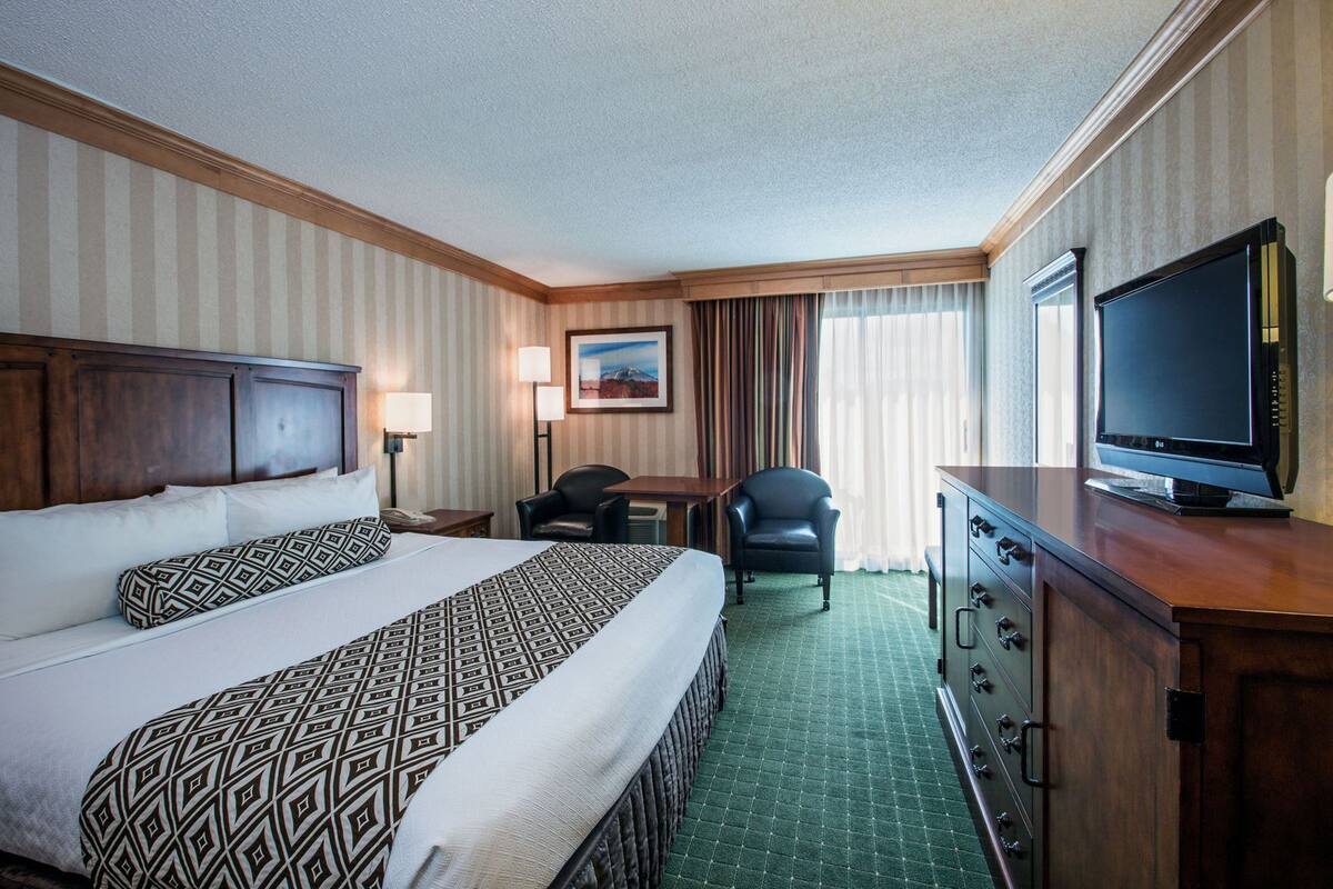 Une chambre d’hôtel avec un grand lit, un bureau, une chaise, une télévision et une commode.