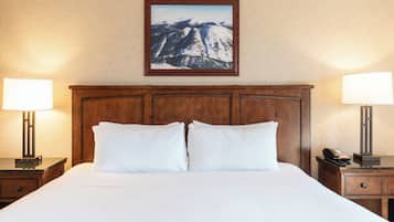 A hotel room with a large bed, two bedside lamps, a wooden headboard, and a framed mountain landscape picture on the wall.