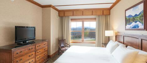 A hotel room with a large bed, a wooden dresser, a television, a chair, a window with a view of mountains, and a painting on the wall.