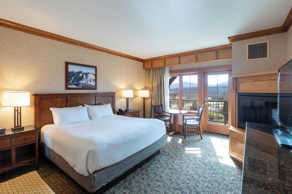 Une chambre d’hôtel avec un grand lit, un bureau avec une chaise, une télévision et une vue sur les montagnes par la fenêtre.