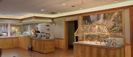 Un hall d’hôtel avec des panneaux de bois, un espace buffet orné d’une fresque représentant une cascade, et un comptoir d’accueil.