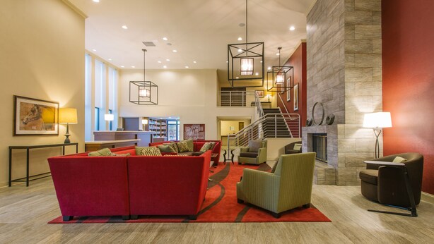 A spacious lobby with a red sofa, green armchairs, a fireplace, and a staircase leading to an upper level. - Hotel MTK Mount Kisco (Mount Kisco)