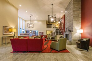 A spacious lobby with a red sofa, green armchairs, a fireplace, and a staircase leading to an upper level. - Hotel MTK Mount Kisco (Mount Kisco)