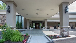 A hotel entrance with a covered walkway, stone pillars, and potted plants. - Hotel MTK Mount Kisco (Mount Kisco)