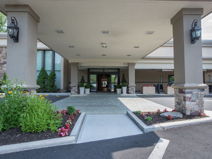 L’entrée d’un hôtel, avec une allée couverte, des piliers en pierre et des plantes en pot.