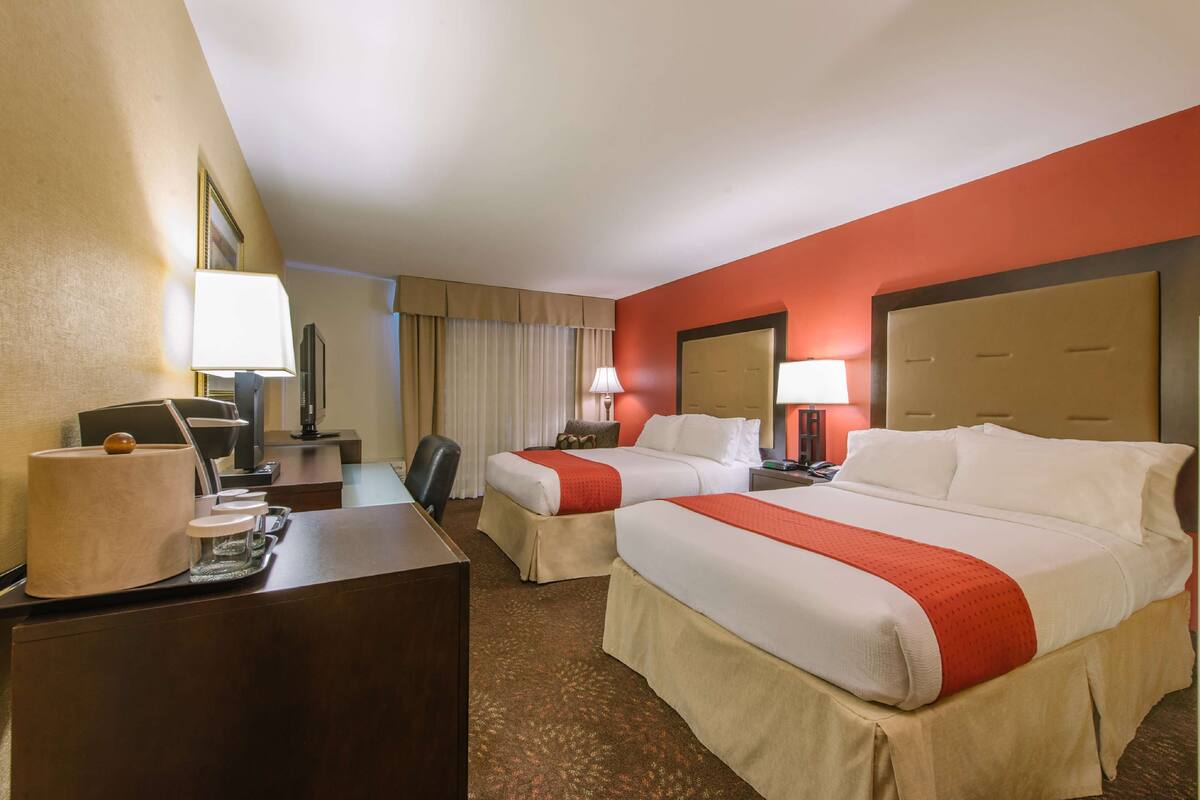 A hotel room with two beds, a desk, a chair, a lamp, and a TV.