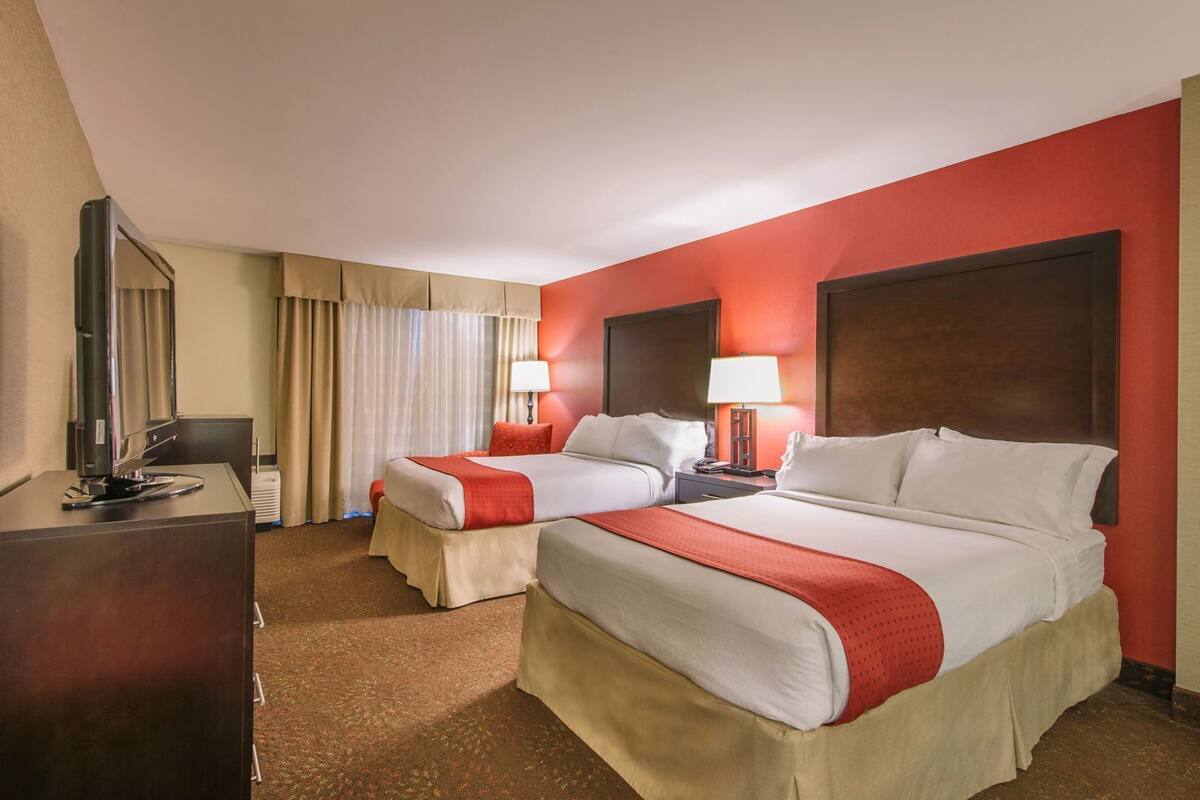 A hotel room with two beds, a desk with a TV, and a window with curtains.