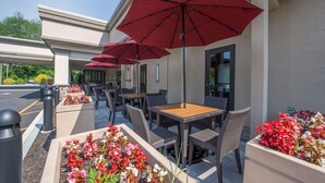 An outdoor patio area with tables and chairs, red umbrellas, and flower planters. - Hotel MTK Mount Kisco (Mount Kisco)