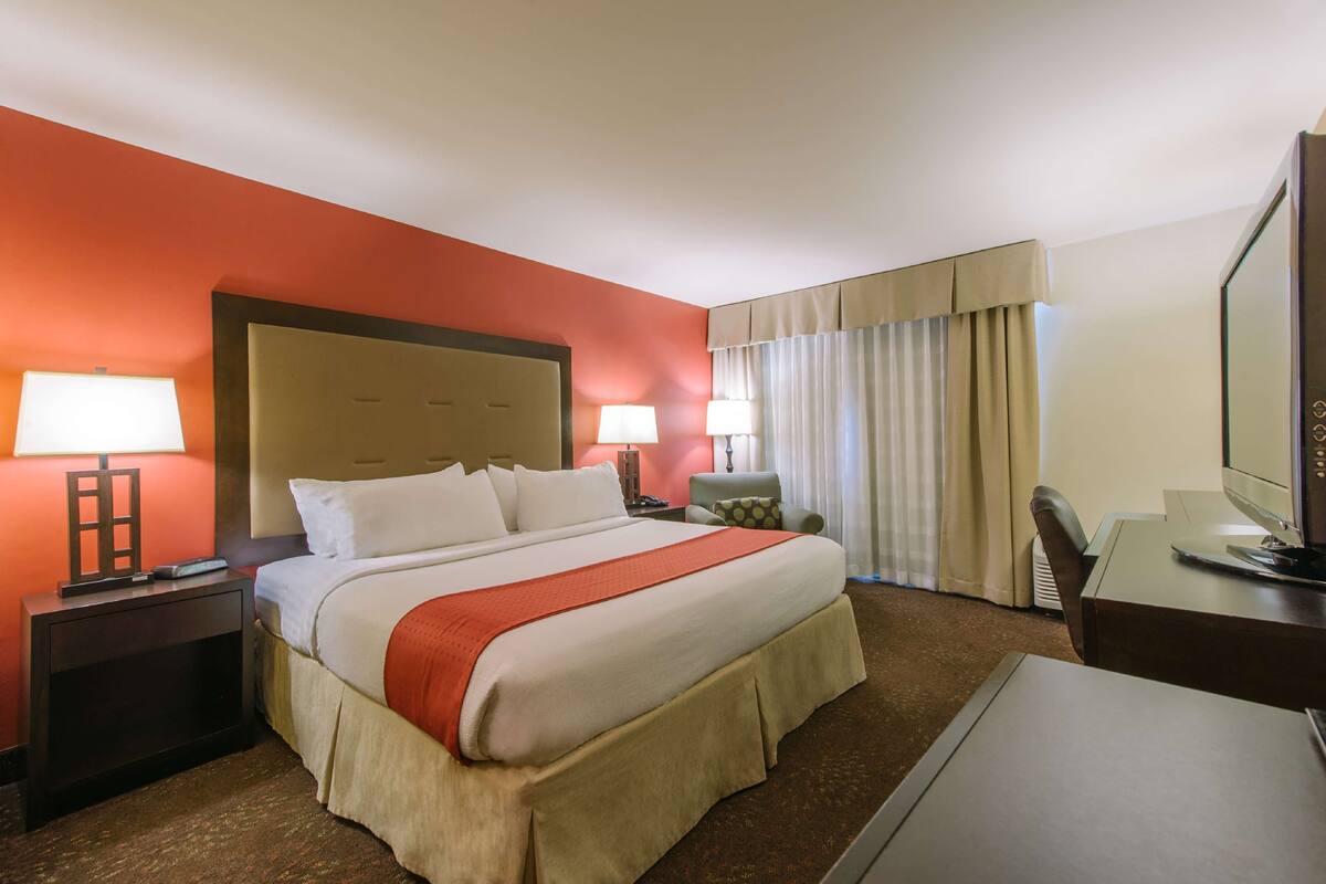 A hotel room with a large bed, two bedside lamps, a desk with a computer, and a television.