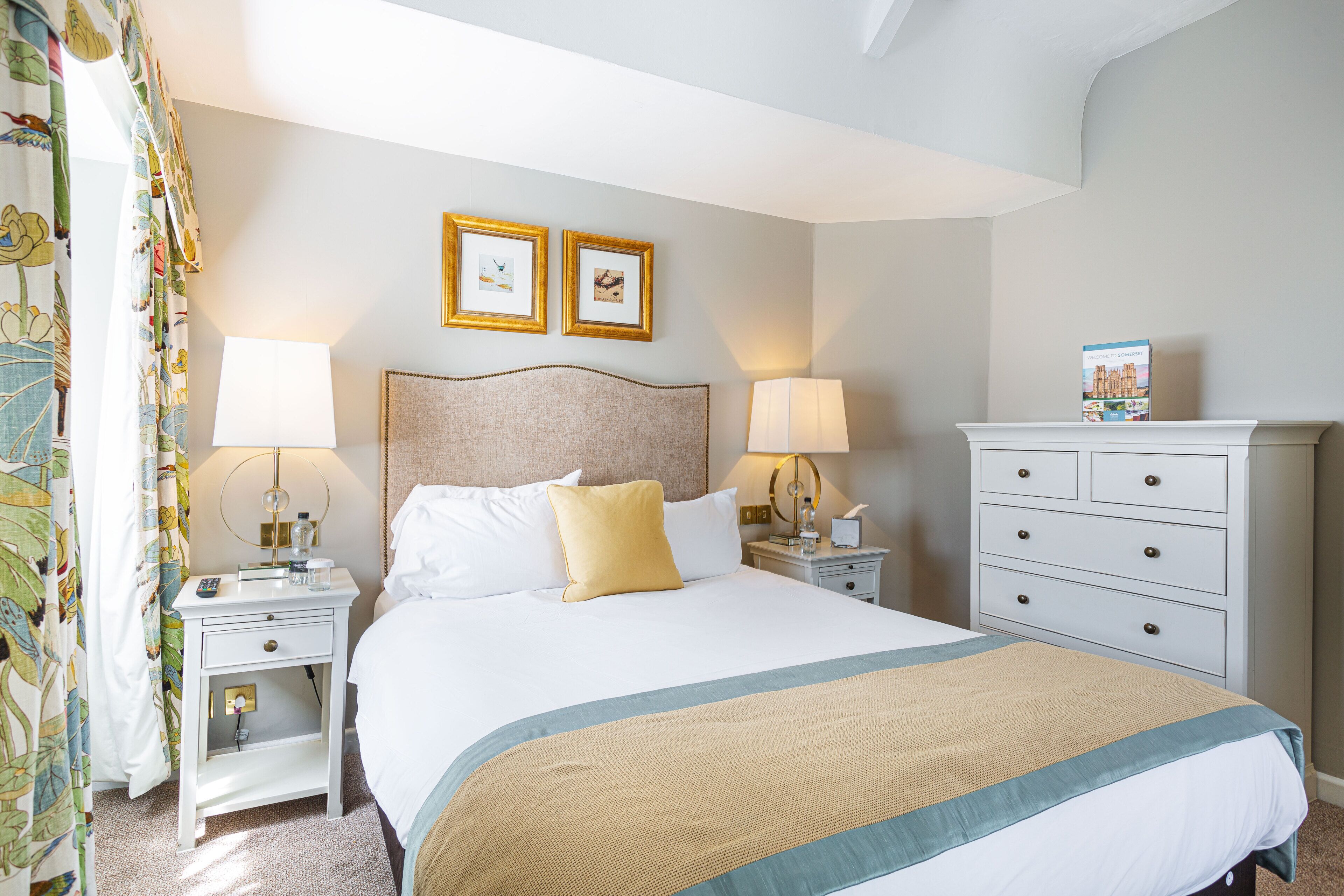 Een hotelkamer met een bed, twee nachtkastjes, een dressoir en twee foto’s in lijsten aan de muur.