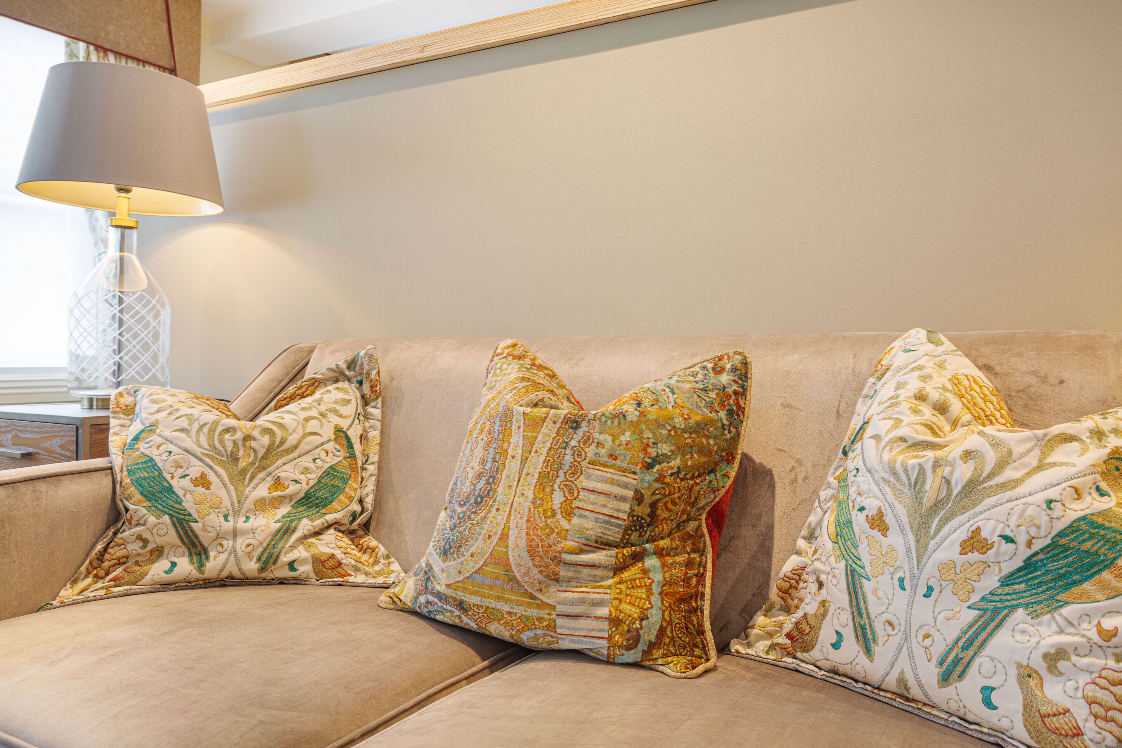 A beige sofa with three patterned cushions, a modern lamp, and a wooden ceiling.