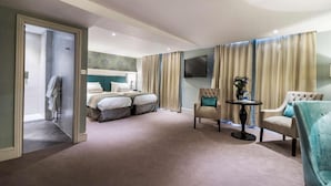 A hotel room with a large bed, a seating area with two chairs, a small table, and a TV mounted on the wall. - The Swan Hotel Wells  (Wells)