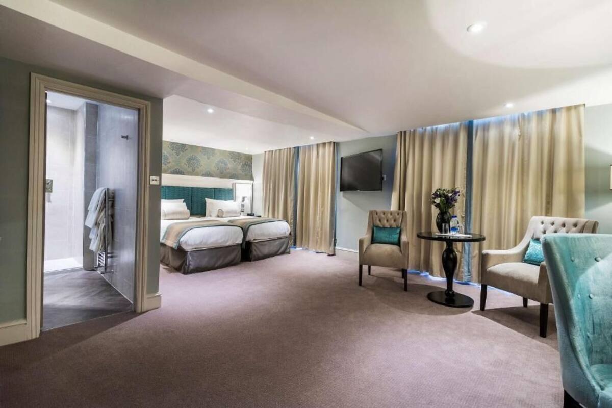 A hotel room with a large bed, a seating area with two chairs, a small table, and a TV mounted on the wall.