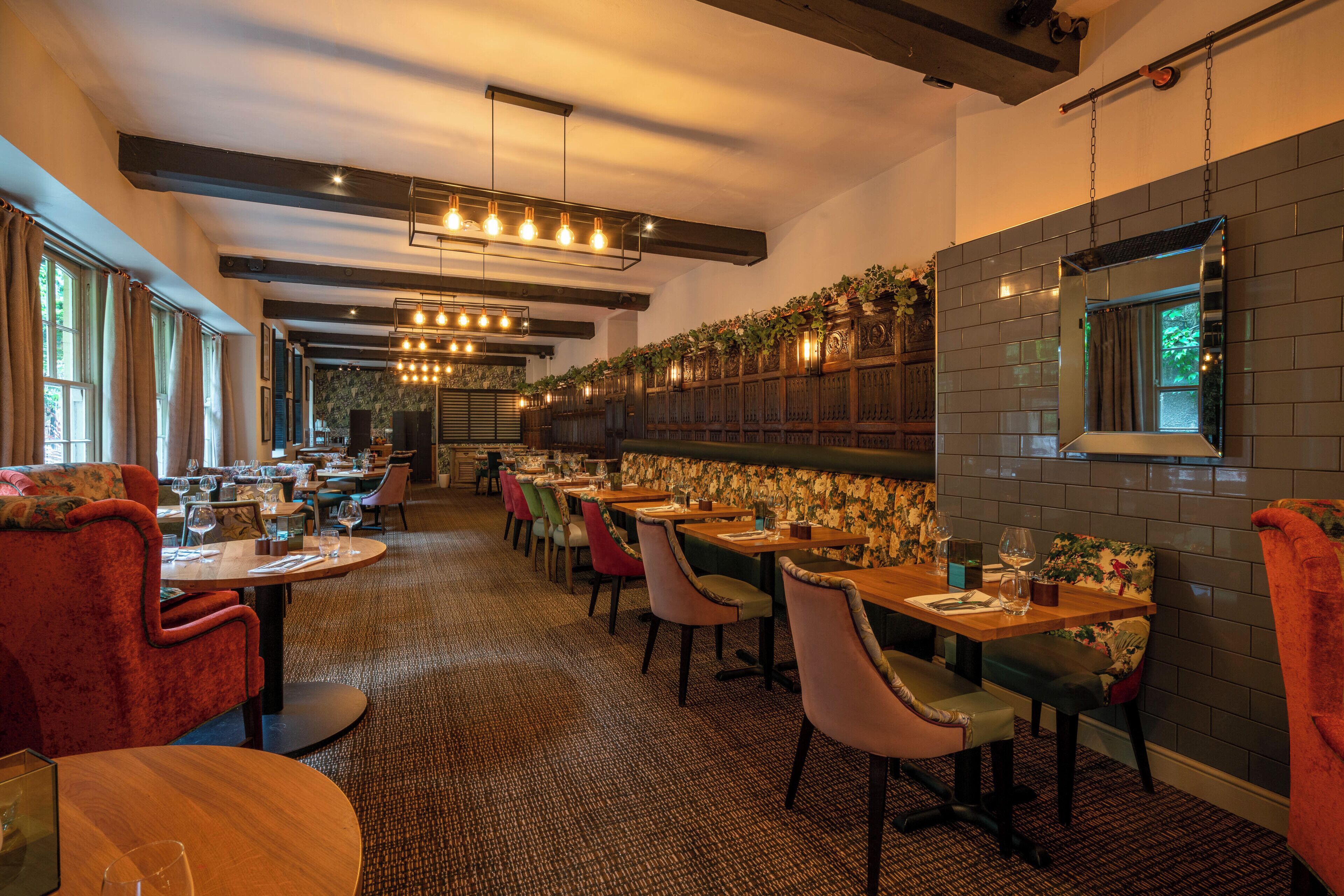 A restaurant with multiple tables and chairs, a patterned wall, and hanging lights.
