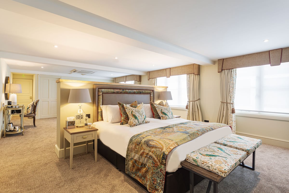 A hotel room with a large bed, bedside tables, a desk, and a window with curtains.