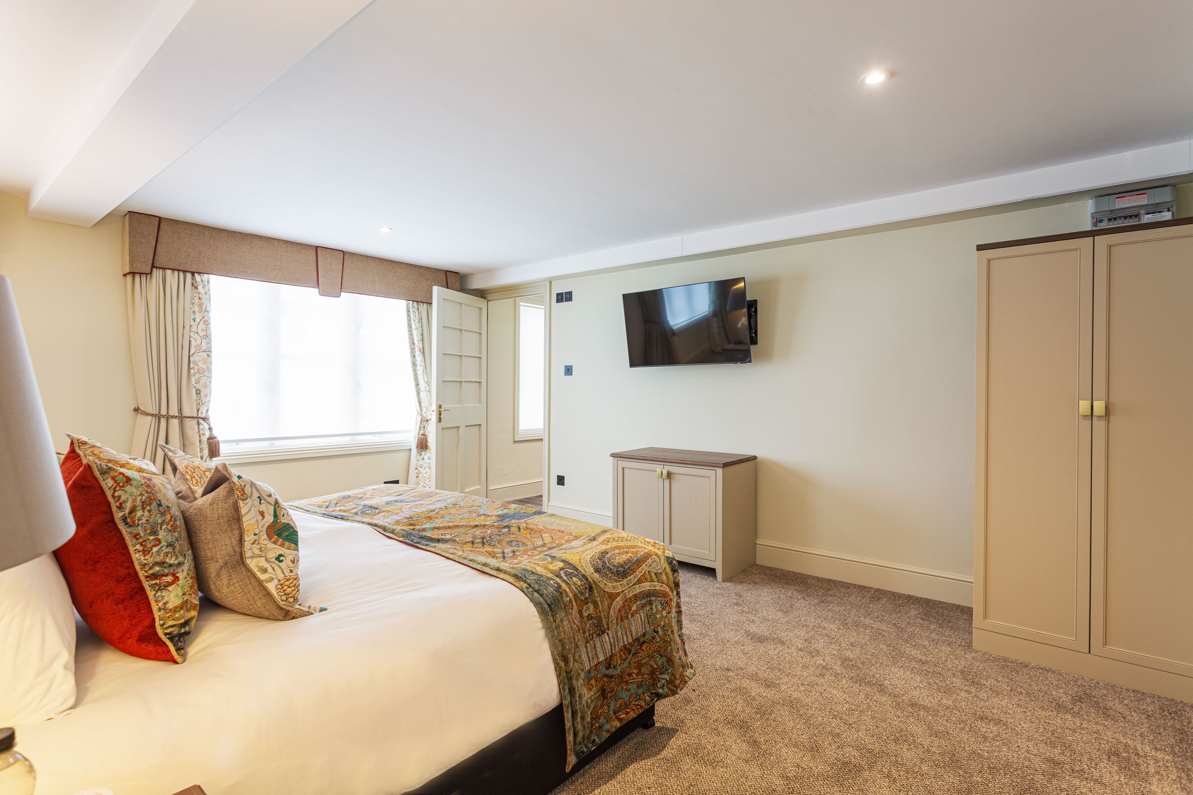 Una camera d'albergo con un letto, una televisione a parete, un armadio e una scrivania.