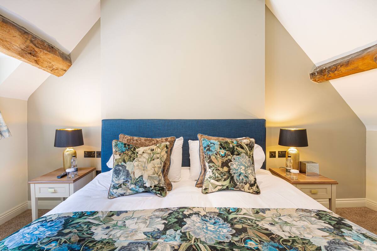 A bedroom with a large bed, two nightstands, a blue headboard, and floral-patterned pillows.