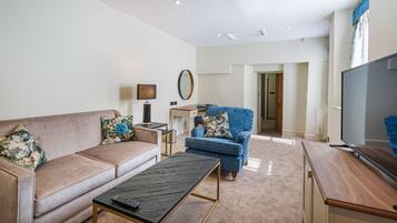 Una sala de estar con sofá, sillón, mesa de centro, televisor y escritorio con lámpara.