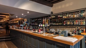 A bar area with a long counter, various bottles, and a menu on the table. - The Swan Hotel Wells  (Wells)