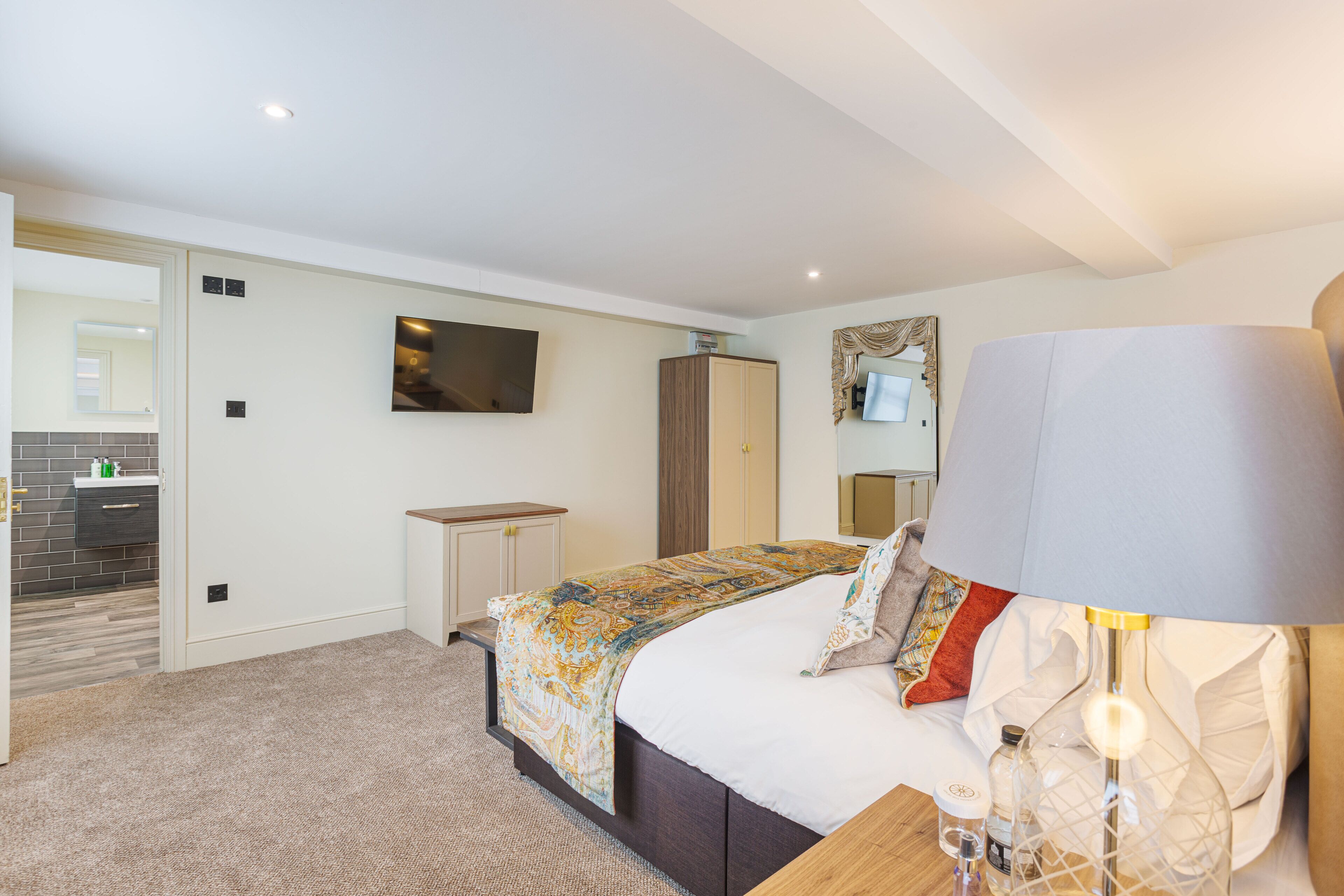 Une chambre à coucher avec un lit, un téléviseur fixé au mur, une armoire et une lampe sur la table de chevet.