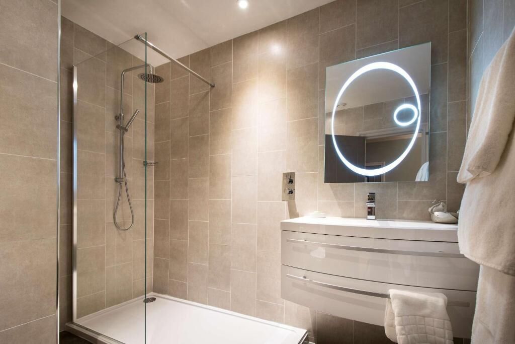 Un baño moderno con ducha de vidrio, tocador con espejo y perchero para toallas.