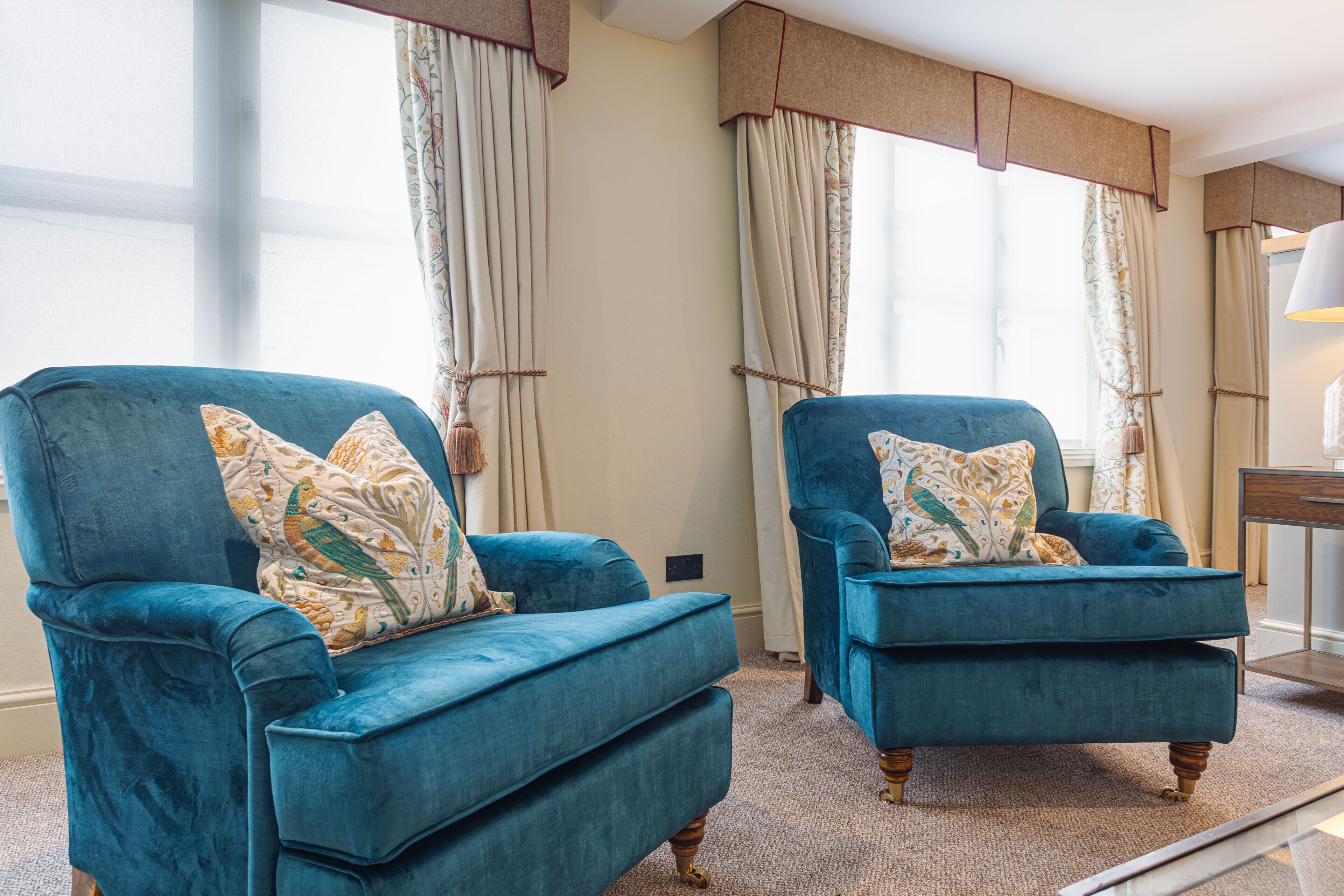 Twee blauwe fauteuils met gestreepte kussens, een houten bijzettafeltje en een lamp.
