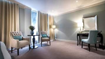 Quarto de hotel com uma janela grande, duas poltronas, uma mesa de trabalho com luminária e um espelho.