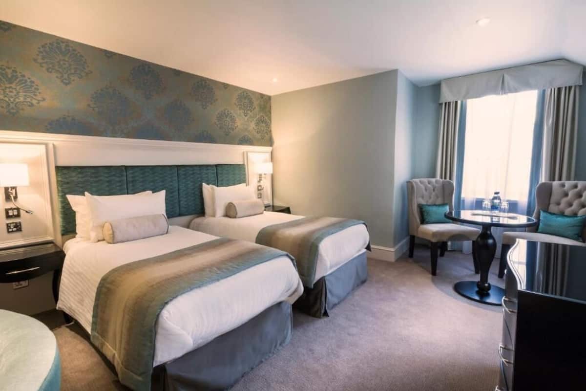 A hotel room with two beds, a small round table, and a chair.
