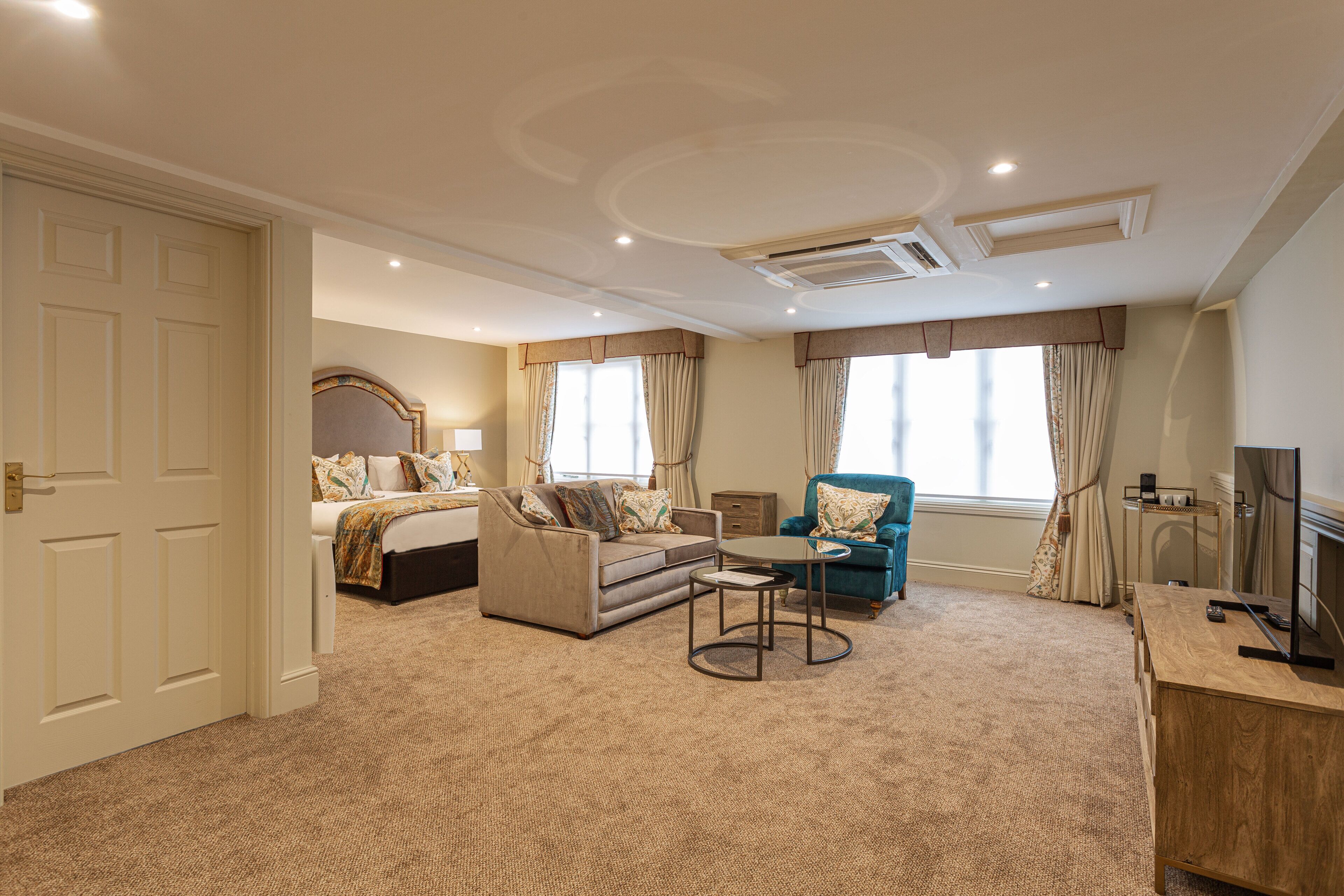 A hotel room with a bed, a sofa, a chair, a small table, a TV, and a fireplace.