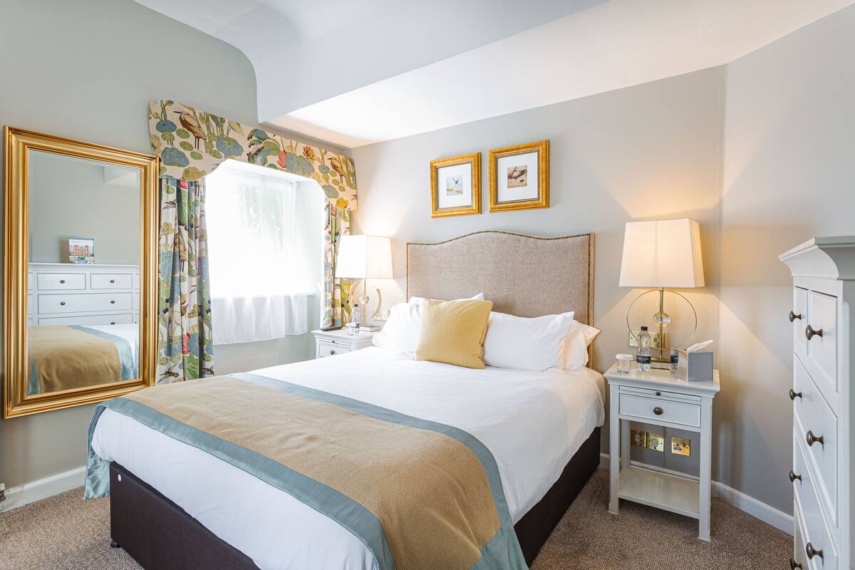 A hotel room with a large bed, two bedside tables, a nightstand, a mirror, and a headboard.