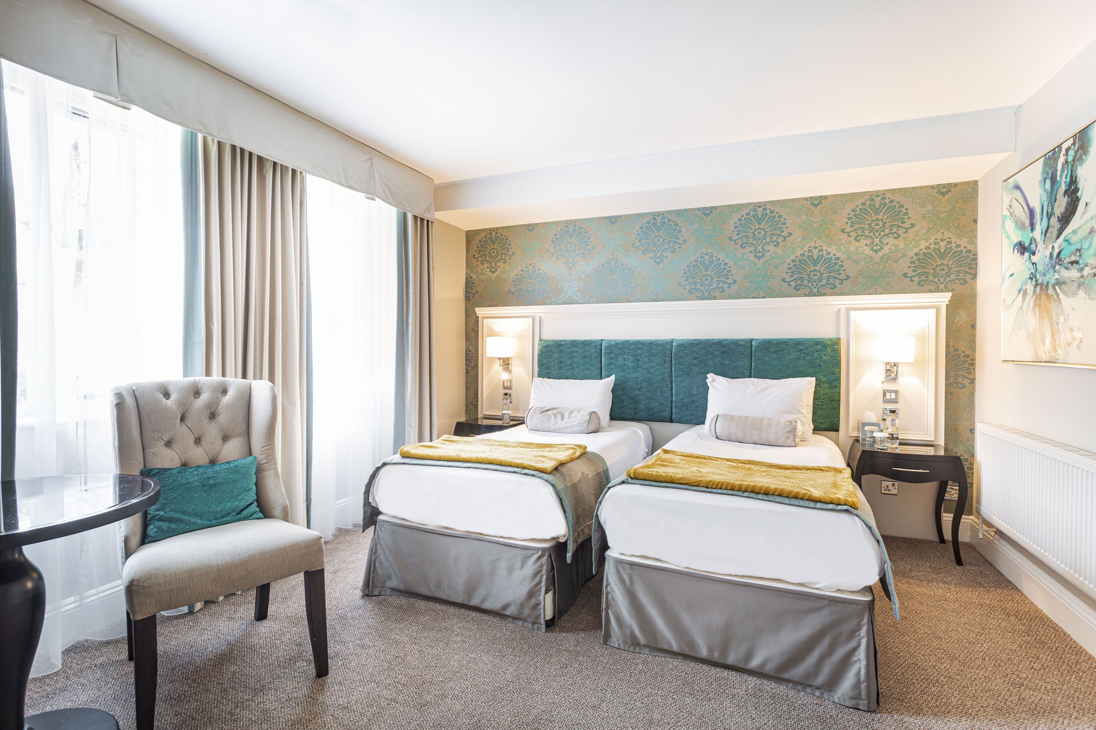 Habitación de hotel con dos camas, una silla, una mesa y vistas a la ciudad.
