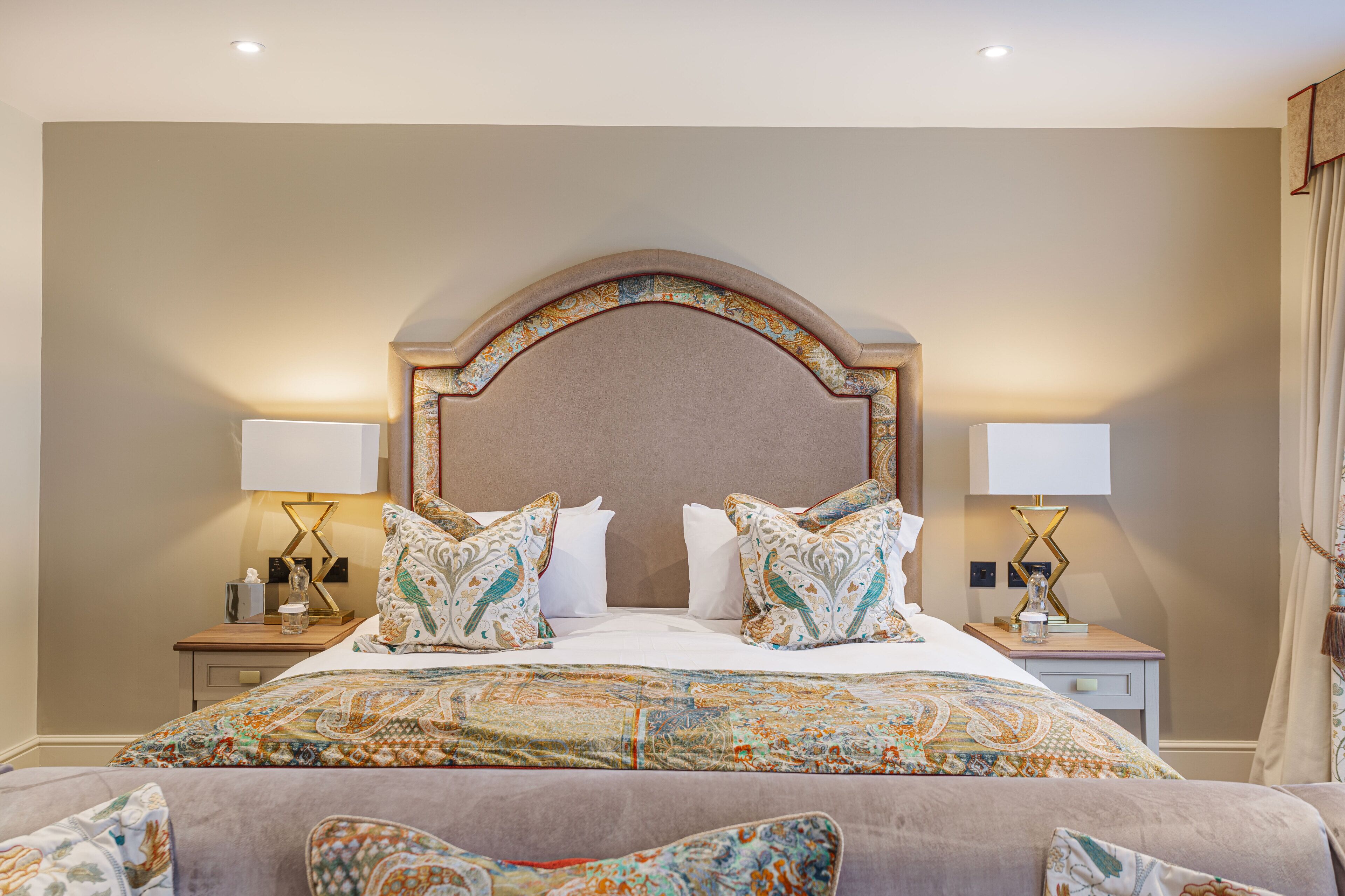 A hotel room with a large bed, two bedside tables, and a headboard with a decorative arch.