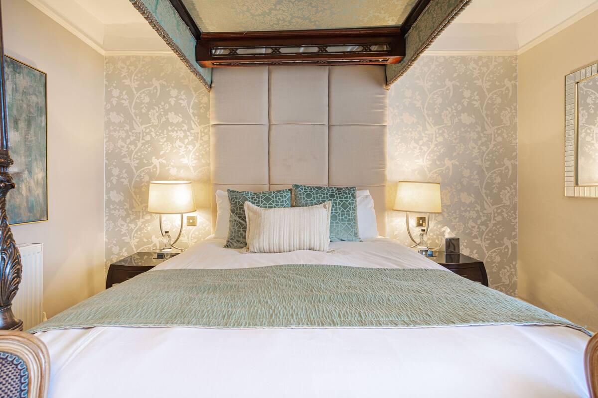 A hotel room with a large bed, two bedside lamps, a headboard, and floral wallpaper.